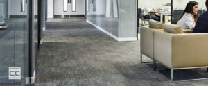 Corporate office building with gray carpet and a woman sitting down off to the right.