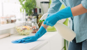 Hands in aqua colored gloves wiping down kitchen counter and spraying liquid