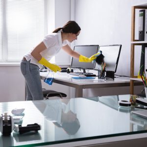 Young woman with yellow gloves on cleaning an office workstation monitor