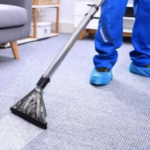 View of cleaner with blue pants and blue shoe protecters on gray carpet steam cleaning floor